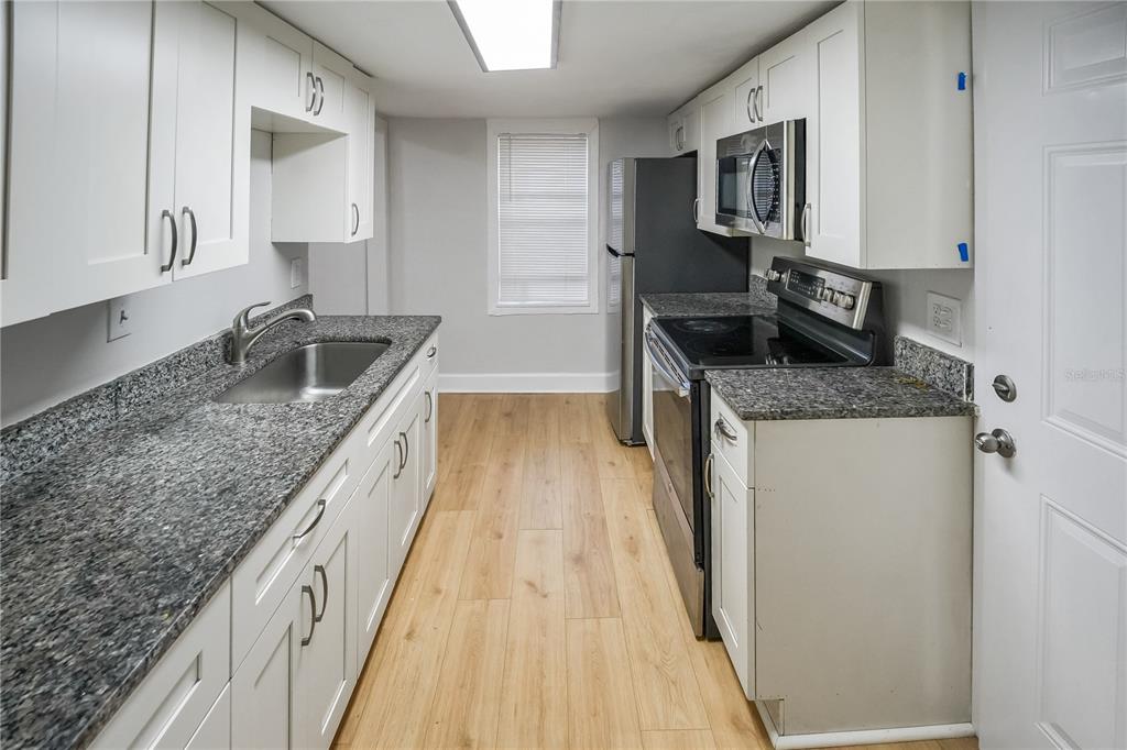 A galley kitchen features white cabinets, granite countertops, stainless steel appliances, and light wood flooring — 8103 N BROOKS STREET, TAMPA, FL