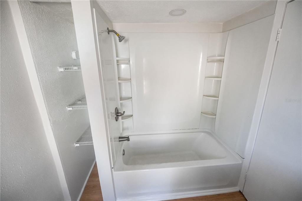 A white bathtub and shower surround with built-in shelving next to an open storage closet — 8103 N BROOKS STREET, TAMPA, FL