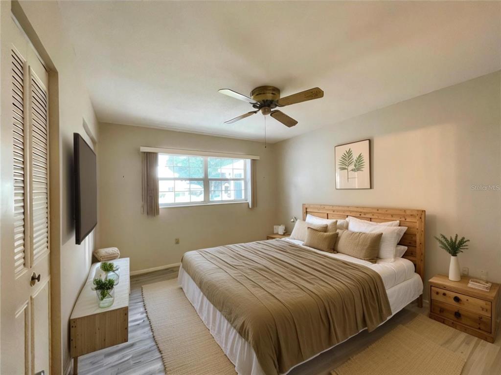 A bedroom features a bed with a wooden headboard, a ceiling fan, and a television — 2687 GOLF COURSE DRIVE UNIT 219, SARASOTA, FL