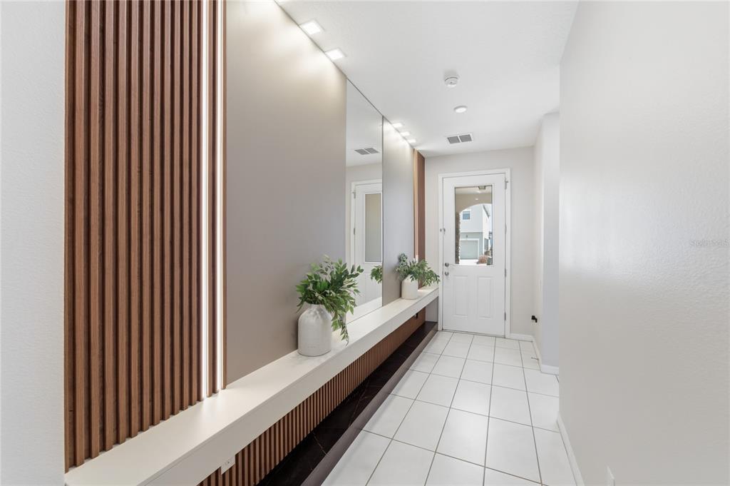 A modern entryway features white tile floors, a wooden slat accent wall, and a floating console — 1860 SAWYER PALM PLACE, KISSIMMEE, FL