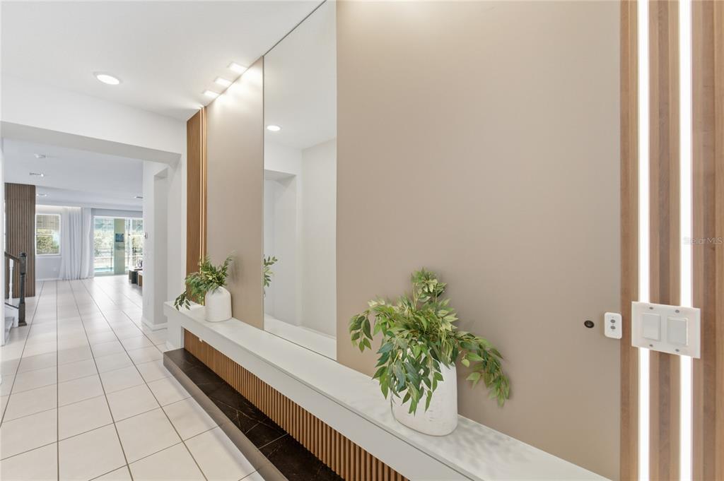 A modern entryway features a long floating console, a large mirror, and vertical wood paneling — 1860 SAWYER PALM PLACE, KISSIMMEE, FL