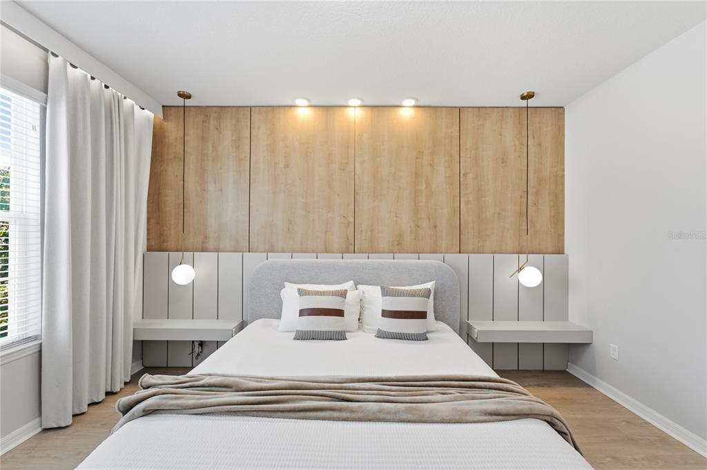 A bedroom features a bed centered against a wood-paneled wall with integrated lighting and nightstands — 1860 SAWYER PALM PLACE, KISSIMMEE, FL