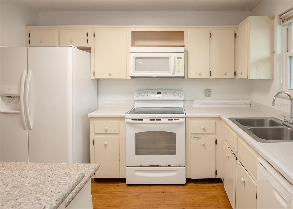 A kitchen features white cabinets, white appliances, a laminate countertop, and wood-look flooring — 2901 N HALIFAX AVENUE UNIT 111, DAYTONA BEACH, FL