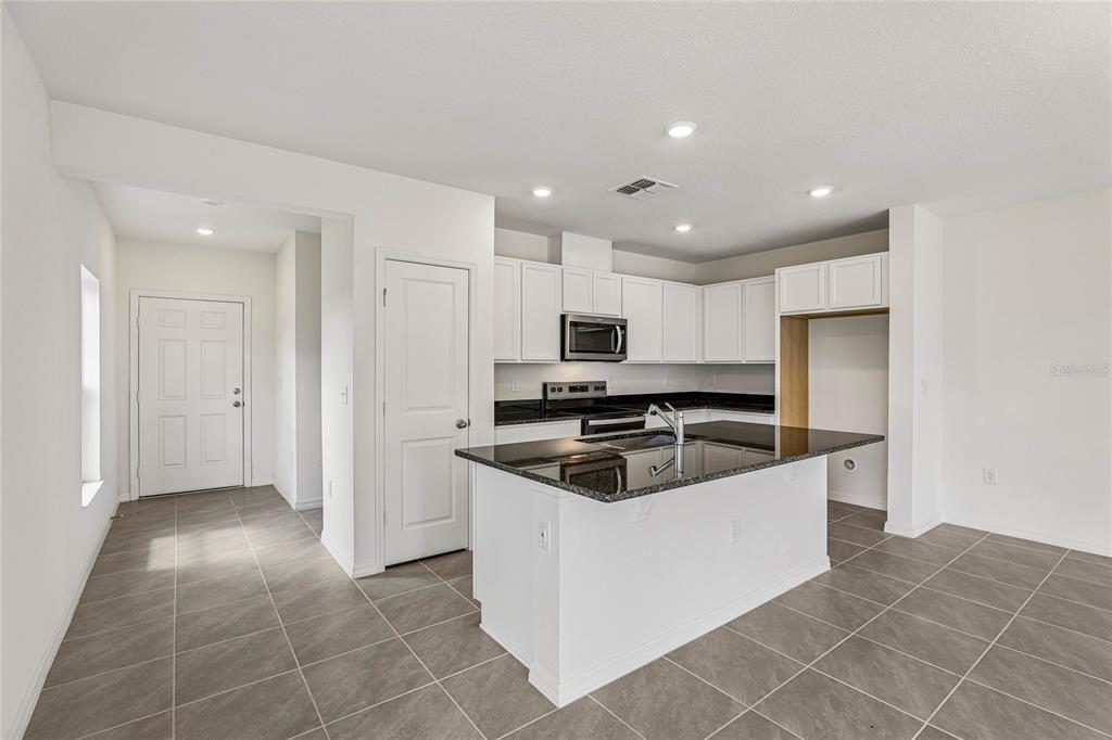 A kitchen with white cabinets, black countertops, a center island, and gray tile flooring — 679 MEADOWS EDGE PLACE, LAKE WALES, FL