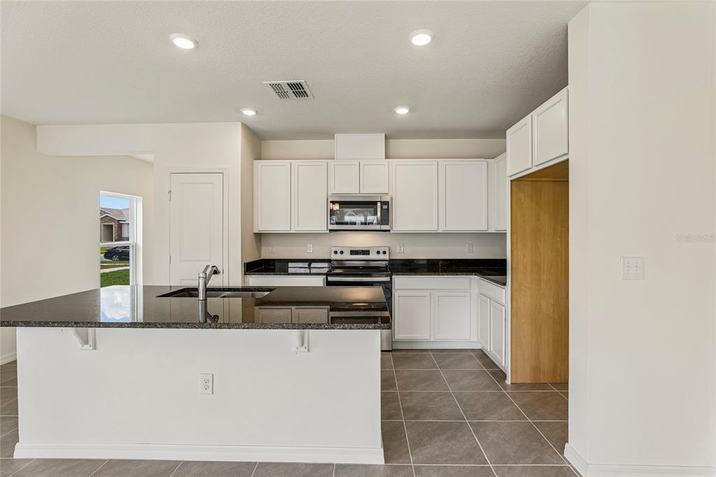 A kitchen features white cabinets, dark granite countertops, a center island, and tile flooring — 679 MEADOWS EDGE PLACE, LAKE WALES, FL