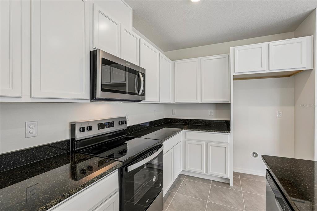 A kitchen features white cabinets, black granite countertops, and stainless steel appliances — 679 MEADOWS EDGE PLACE, LAKE WALES, FL