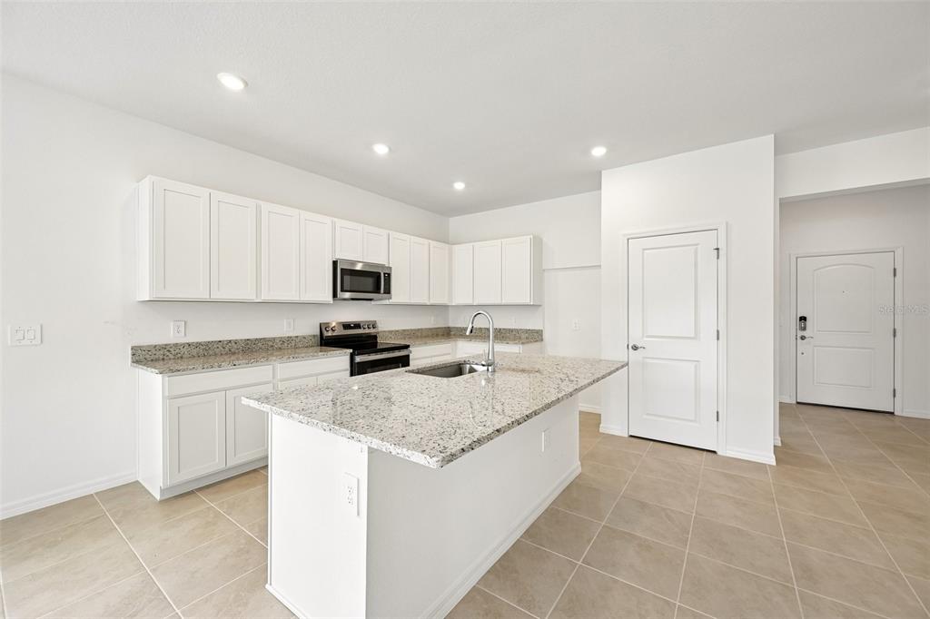 A kitchen features white cabinets, granite countertops, a center island, and light tile flooring — 4422 OUTHAUL RUN, PALMETTO, FL