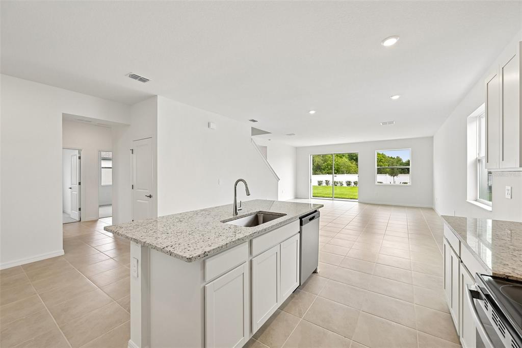 A kitchen with a granite-topped island and white cabinets overlooks an open-concept living area — 4422 OUTHAUL RUN, PALMETTO, FL