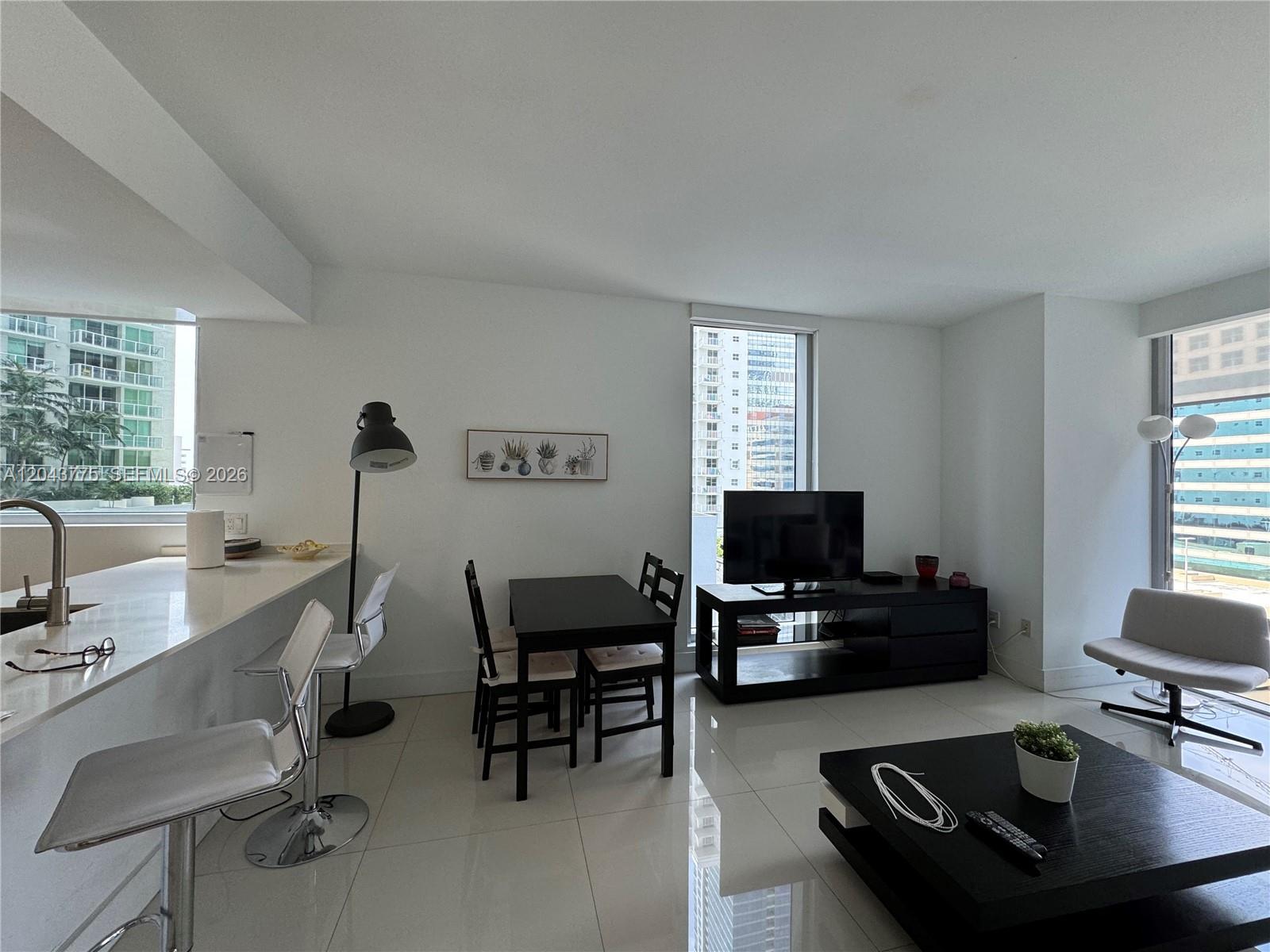 A modern living and dining area features white tile floors, white walls, and city views — 1300 Brickell Bay Dr # 901, Miami FL 33131, MIAMI, FL