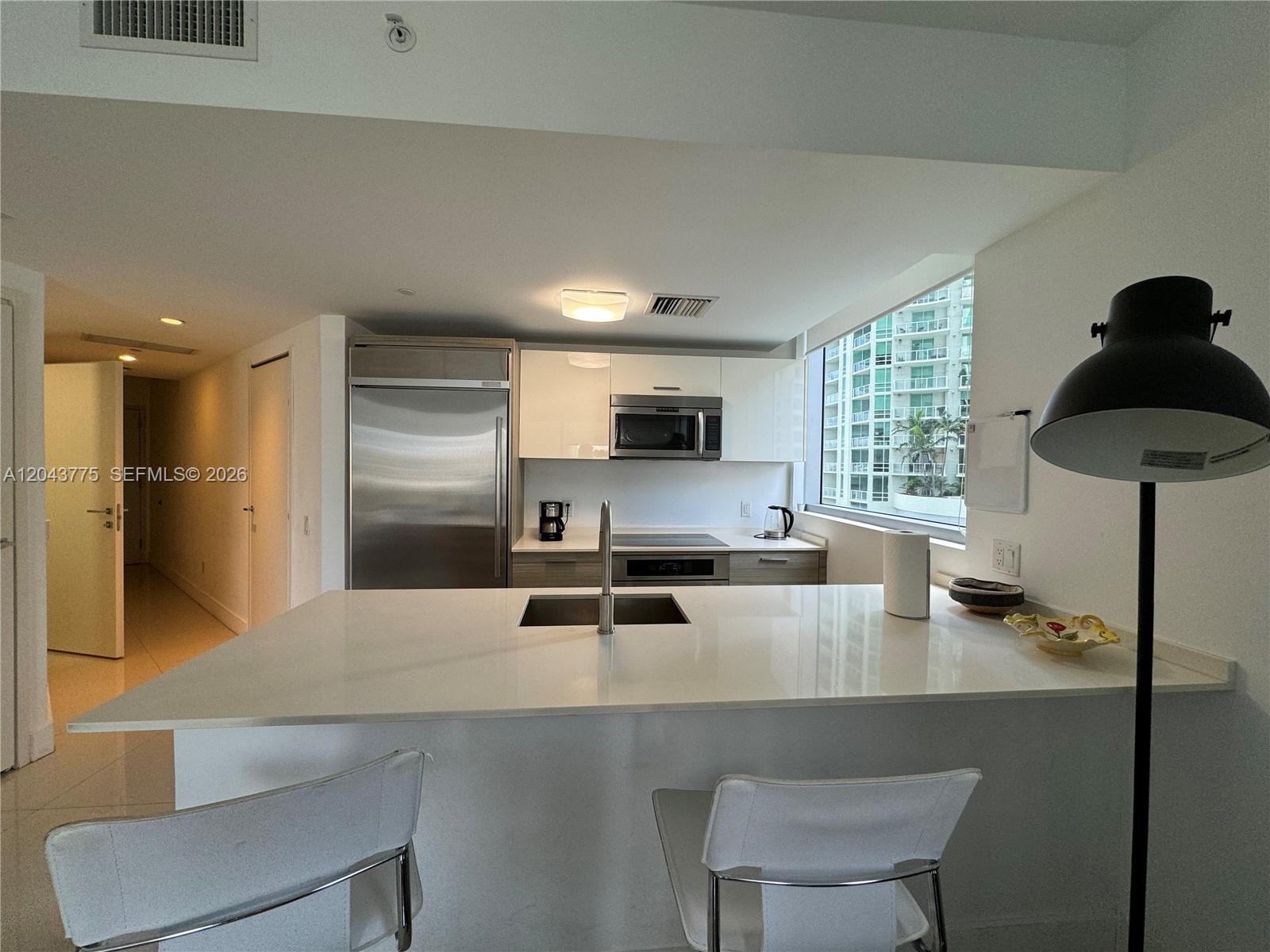 A modern kitchen features white cabinetry, stainless steel appliances, and a central island with seating — 1300 Brickell Bay Dr # 901, Miami FL 33131, MIAMI, FL