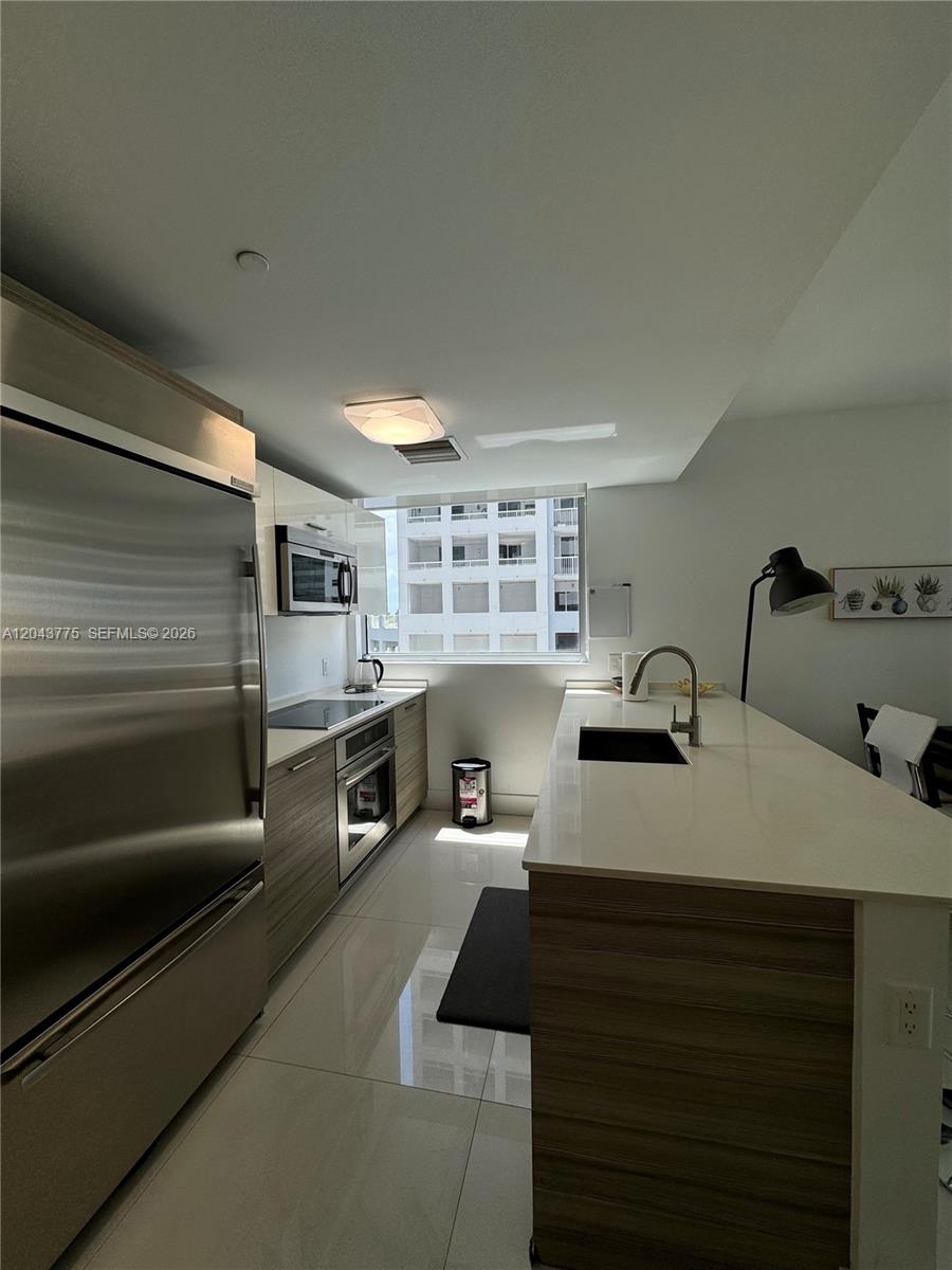 A modern kitchen features stainless steel appliances, wood-grain cabinetry, and a white quartz island — 1300 Brickell Bay Dr # 901, Miami FL 33131, MIAMI, FL