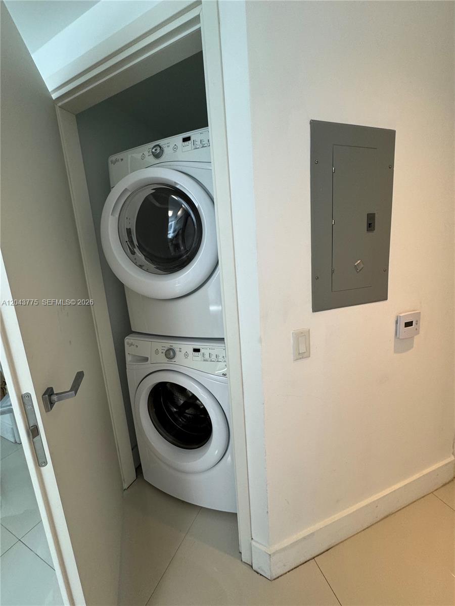 A stacked washer and dryer unit sits inside a closet next to an electrical panel — 1300 Brickell Bay Dr # 901, Miami FL 33131, MIAMI, FL