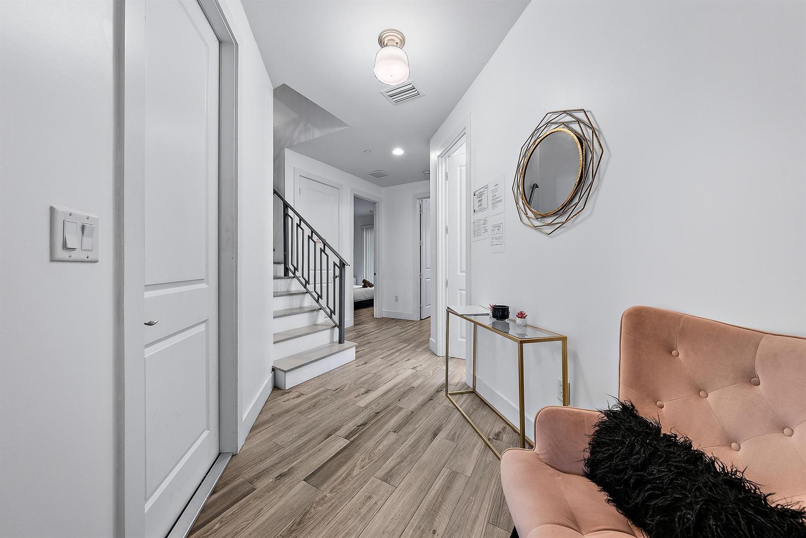 A hallway features light wood-look flooring, a staircase with a metal railing, and a pink chair — 3770 County Line Road # C1, Tequesta FL 33469, TEQUESTA, FL
