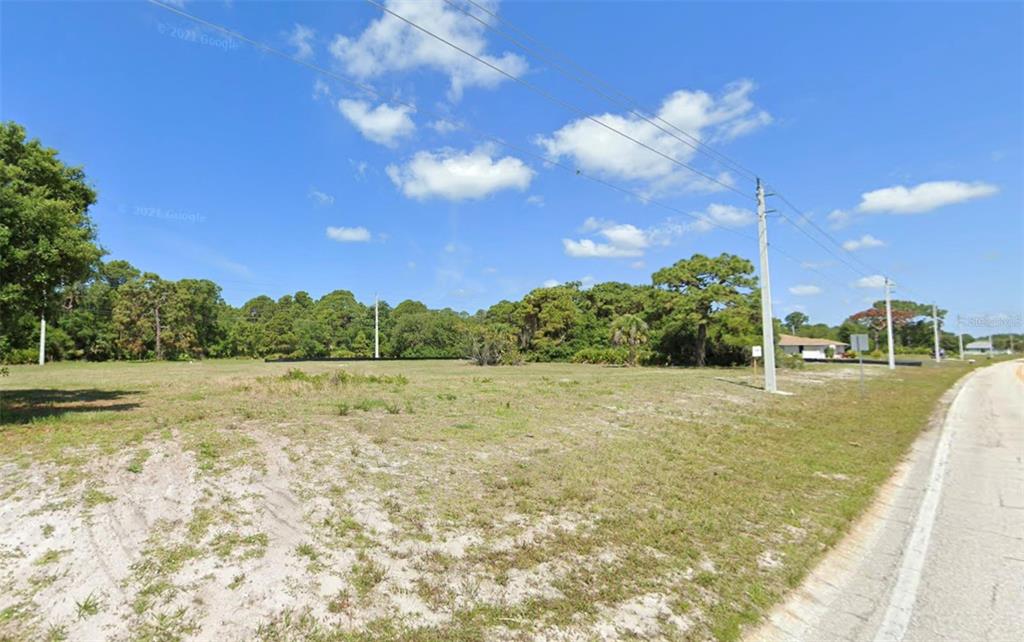 A vacant, grassy lot sits beside a paved road under a blue sky with clouds — 121 & 123 BOUNDARY BOULEVARD, ROTONDA WEST, FL