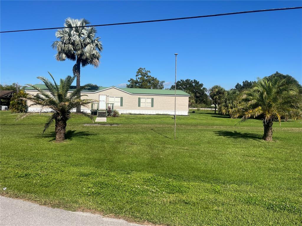 A single-story manufactured home sits on a grassy lot with several palm trees — 1145 YAUN ROAD, MOORE HAVEN, FL