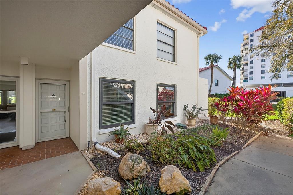 A two-story stucco building exterior features a front entrance, windows, and a landscaped garden — 6210 SUN BOULEVARD UNIT 112, ST PETERSBURG, FL