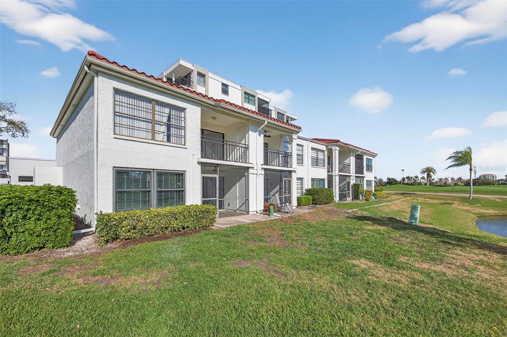 A multi-story apartment building with screened balconies overlooks a grassy lawn and a small pond — 6210 SUN BOULEVARD UNIT 112, ST PETERSBURG, FL