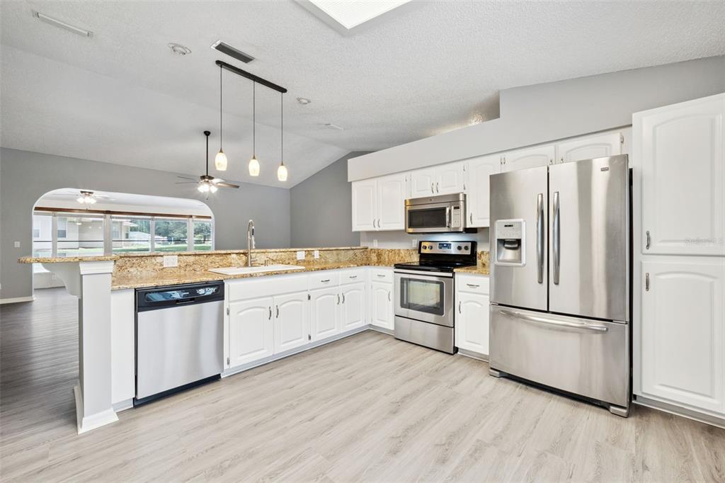 A kitchen with white cabinets, stainless steel appliances, granite countertops, and light wood-look flooring — 6419 BORG STREET, LEESBURG, FL