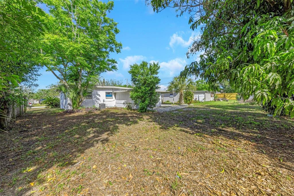 A view of a backyard with a white house, mature trees, and a concrete patio — 4040 FLAMINGO DRIVE, NEW PORT RICHEY, FL