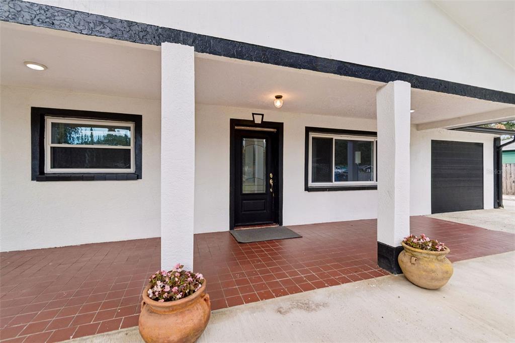 A covered porch with red tile flooring, white columns, and a black front door — 5712 20TH AVENUE S, TAMPA, FL