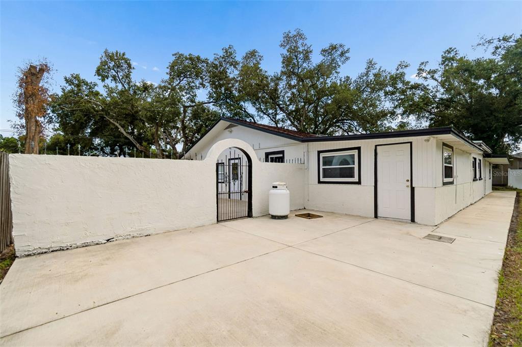 A white exterior wall with an arched gate and a concrete driveway beside a house — 5712 20TH AVENUE S, TAMPA, FL