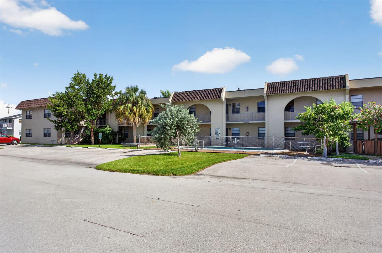An exterior view of a multi-story apartment building with a pool and parking lot — 2141 NE 42nd Street # 112, Lighthouse Point FL 33064, LIGHTHOUSE POINT, FL
