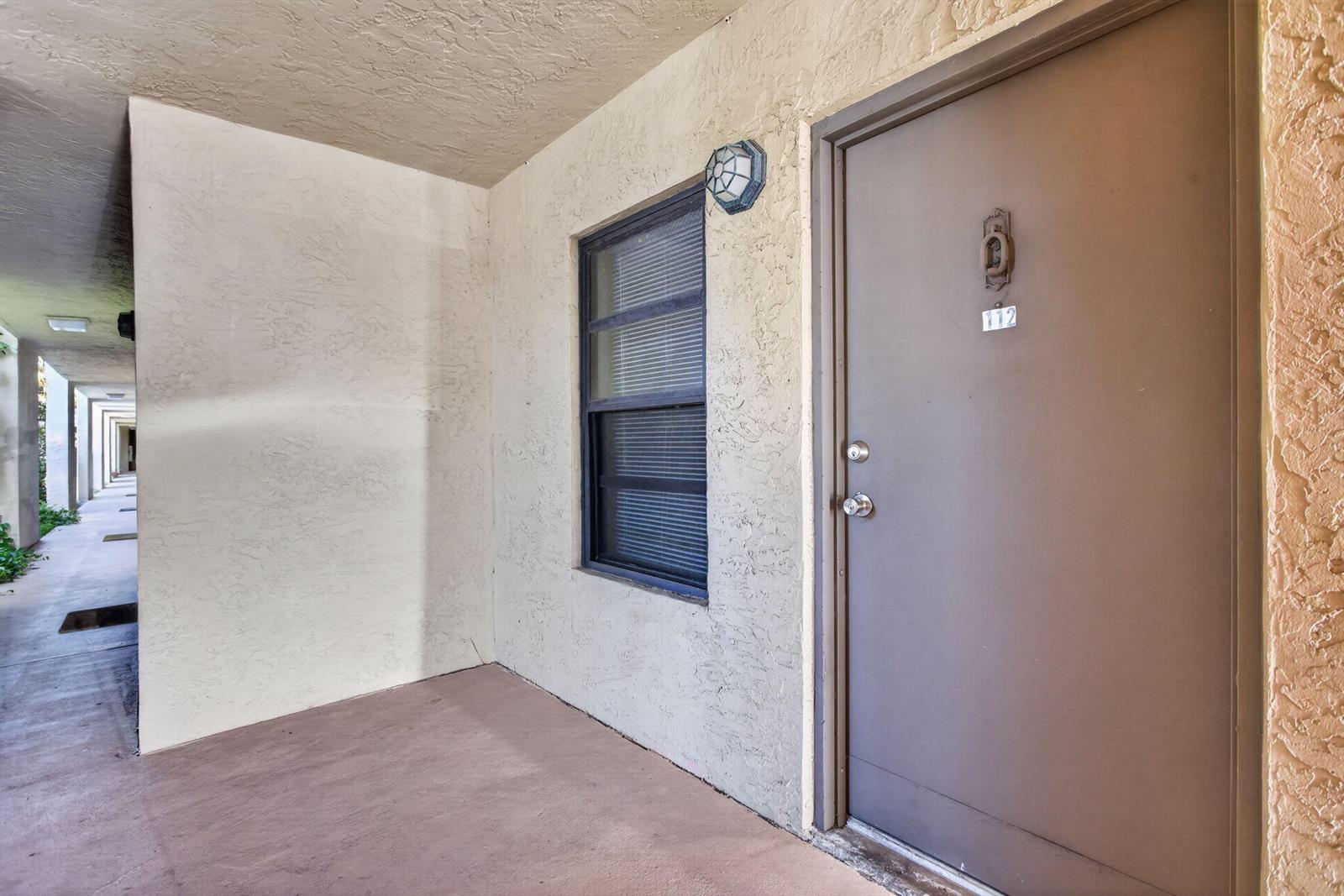 An exterior view of a building entrance featuring a brown door numbered 112 — 2141 NE 42nd Street # 112, Lighthouse Point FL 33064, LIGHTHOUSE POINT, FL