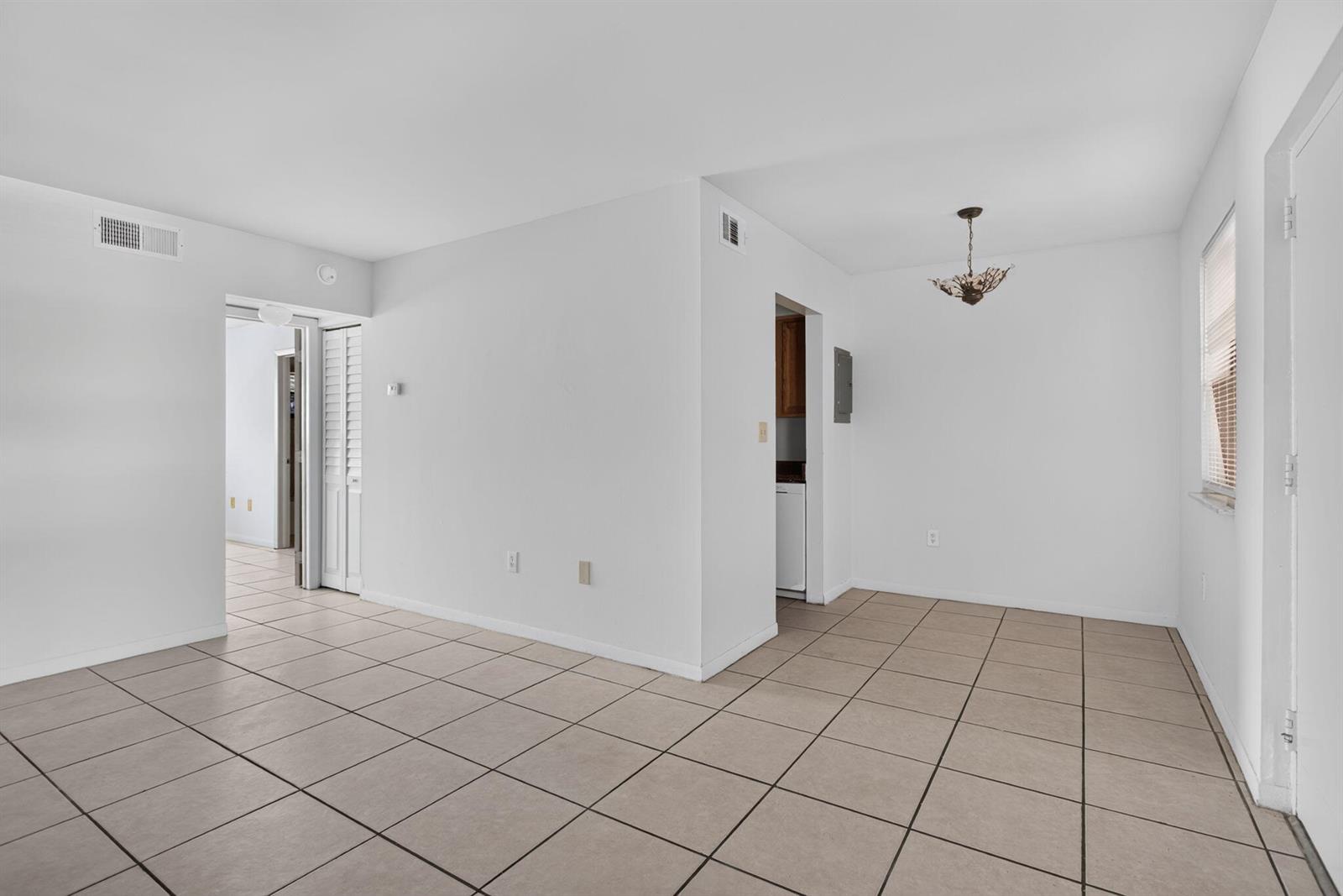 An empty room with white walls, beige tile flooring, and a dining area light fixture — 2141 NE 42nd Street # 112, Lighthouse Point FL 33064, LIGHTHOUSE POINT, FL
