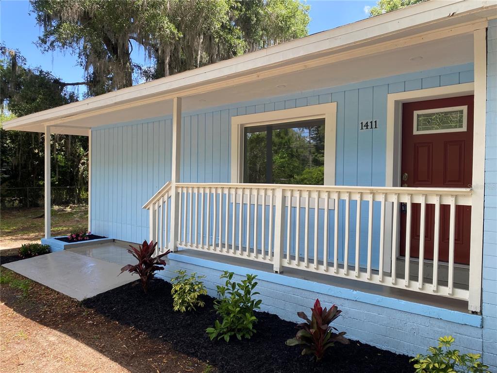 A light blue house exterior features a white porch railing, a red door, and landscaping — 1411 SE 35TH ST, GAINESVILLE, FL