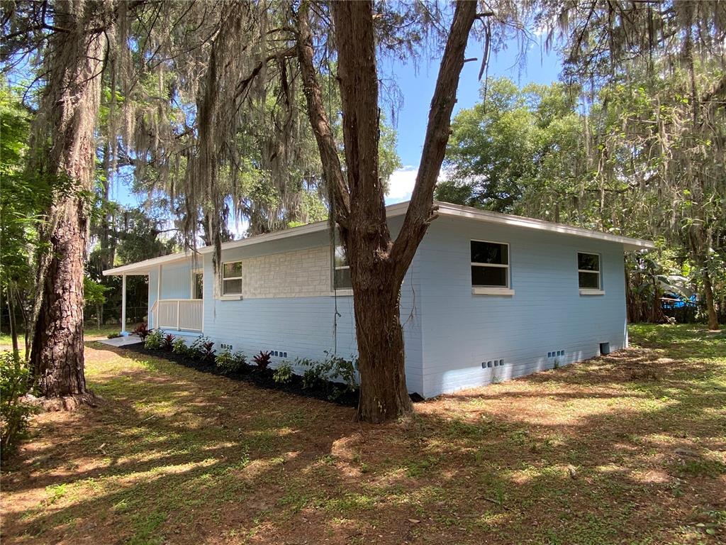 A light blue, single-story house with a white stone accent wall sits among mossy trees — 1411 SE 35TH ST, GAINESVILLE, FL