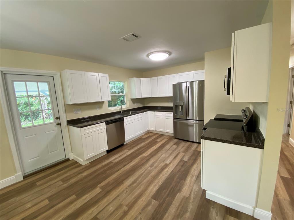 A kitchen features white cabinets, dark countertops, stainless steel appliances, and wood-look flooring — 1411 SE 35TH ST, GAINESVILLE, FL