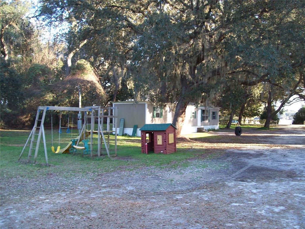 A mobile home sits on a dirt lot with a wooden playset and small playhouse — 6382 BAKER ROAD, KEYSTONE HEIGHTS, FL