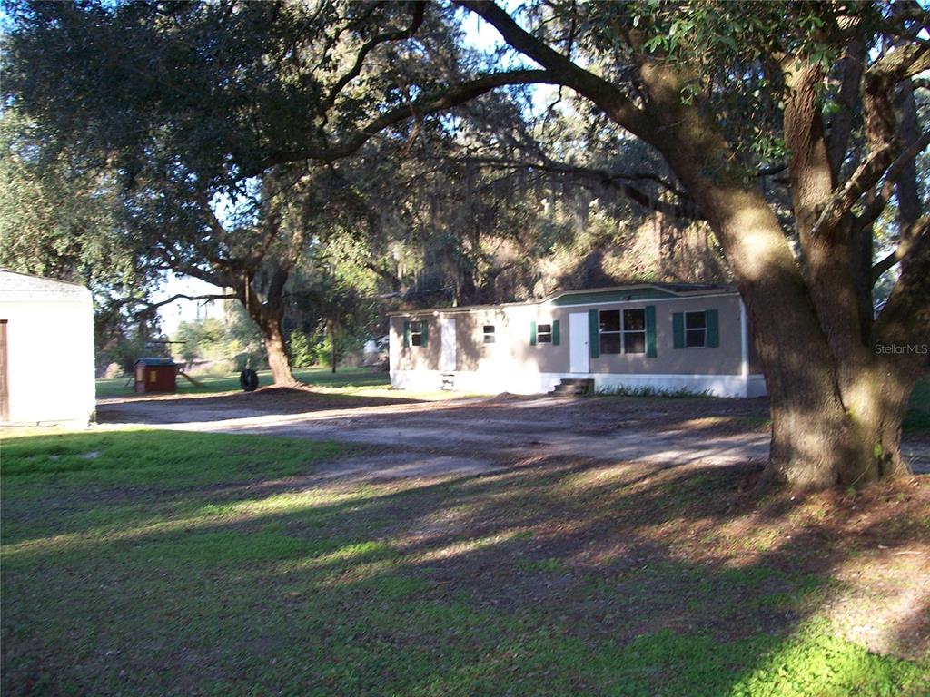 A single-story manufactured home sits on a dirt lot shaded by large oak trees — 6382 BAKER ROAD, KEYSTONE HEIGHTS, FL