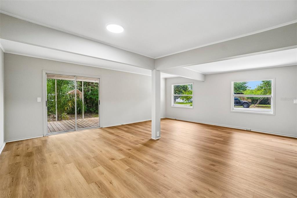 An empty living room features light wood-look flooring, white walls, a support column, and windows — 620 2ND STREET, POLK CITY, FL