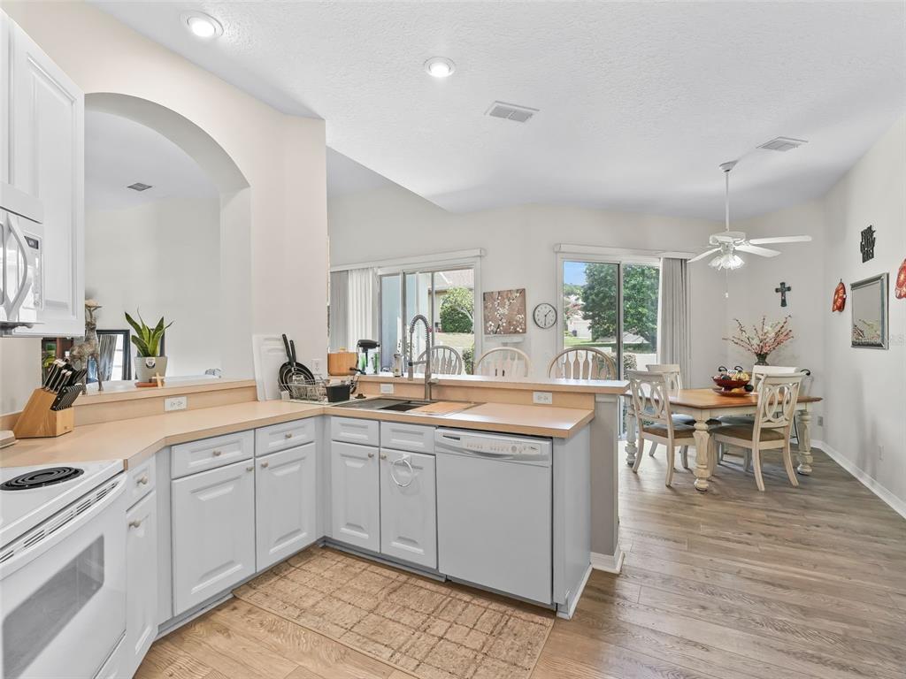 A kitchen with white cabinets and light countertops opens to a dining area with wood flooring — 17435 SE 112TH AVENUE, SUMMERFIELD, FL