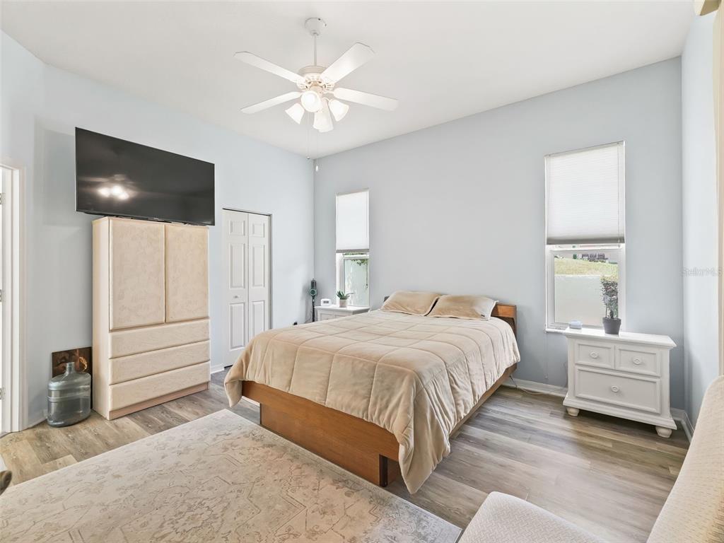 A bedroom features a bed, a tall dresser with a television, and light-colored wood flooring — 17435 SE 112TH AVENUE, SUMMERFIELD, FL