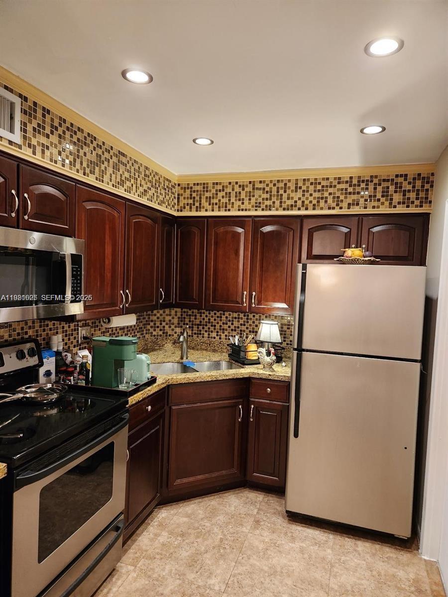A kitchen features dark wood cabinets, granite countertops, a tiled backsplash, and stainless steel appliances — 9 NE 19th Ct # 208C, Wilton Manors FL 33305, WILTON MANORS, FL