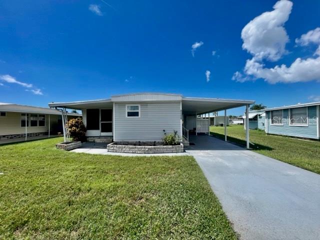A single-story manufactured home features light gray siding, a carport, and a front garden bed — 10819 LONDON DRIVE, PORT RICHEY, FL