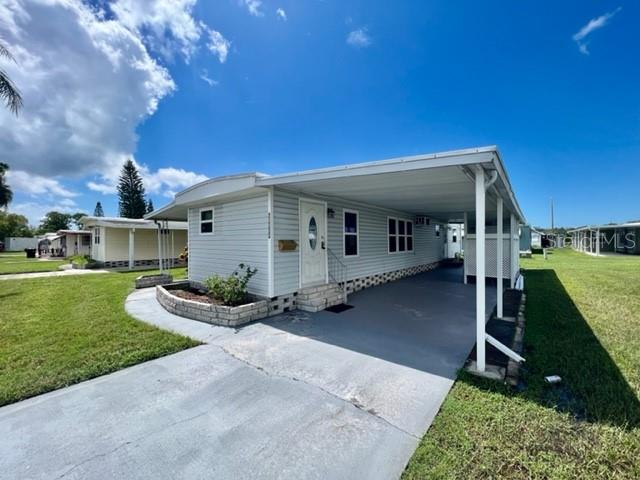 A light-colored mobile home features a covered carport and a small landscaped garden bed — 10819 LONDON DRIVE, PORT RICHEY, FL