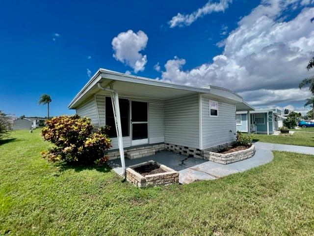 A light-colored mobile home features a covered patio area and a small brick planter box — 10819 LONDON DRIVE, PORT RICHEY, FL
