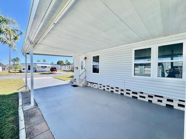 A covered concrete carport sits beside the white siding of a mobile home — 10819 LONDON DRIVE, PORT RICHEY, FL