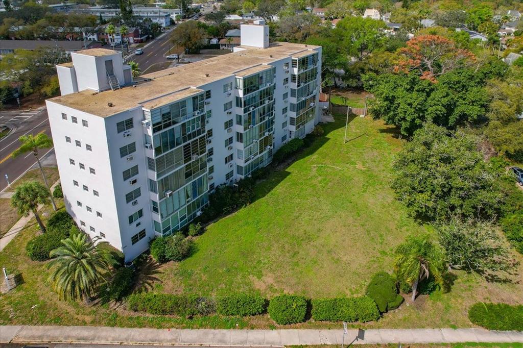 An aerial view shows a multi-story white apartment building next to a large grassy lot — 200 N BETTY LANE UNIT 1C, CLEARWATER, FL