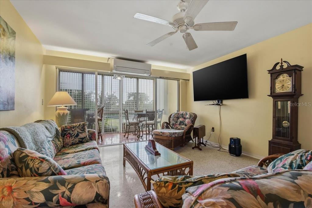 A living room features floral furniture, a glass coffee table, a grandfather clock, and sliding doors — 200 N BETTY LANE UNIT 1C, CLEARWATER, FL
