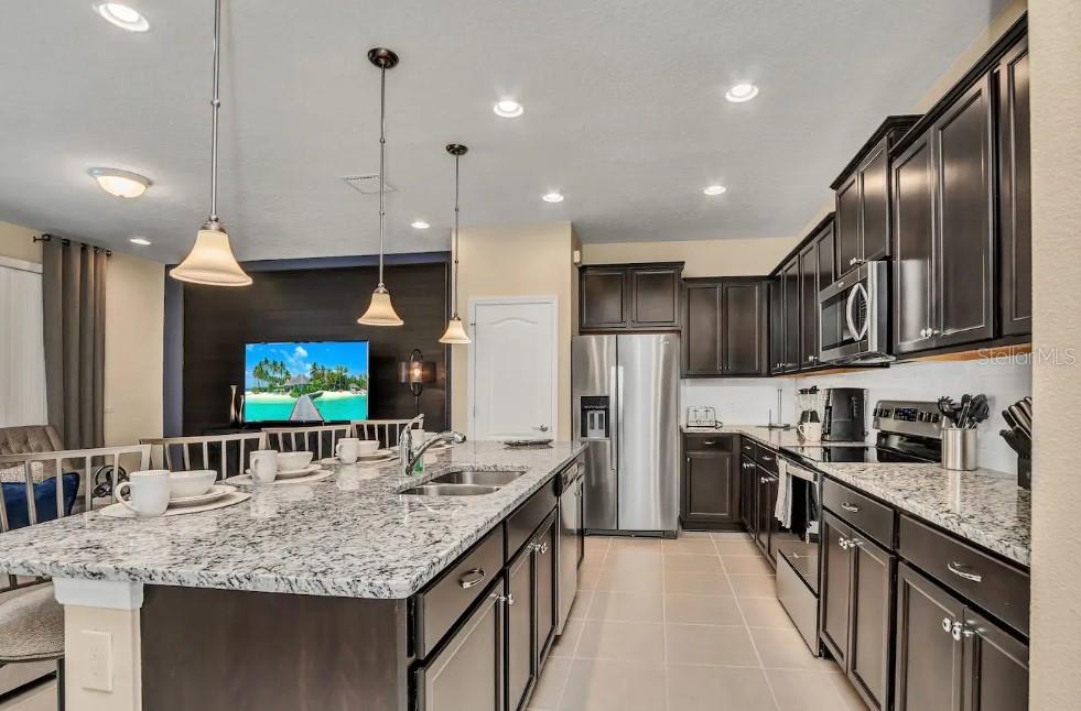 A kitchen with dark wood cabinets, granite countertops, a large island, and stainless steel appliances — 2407 DUBAI STREET, KISSIMMEE, FL