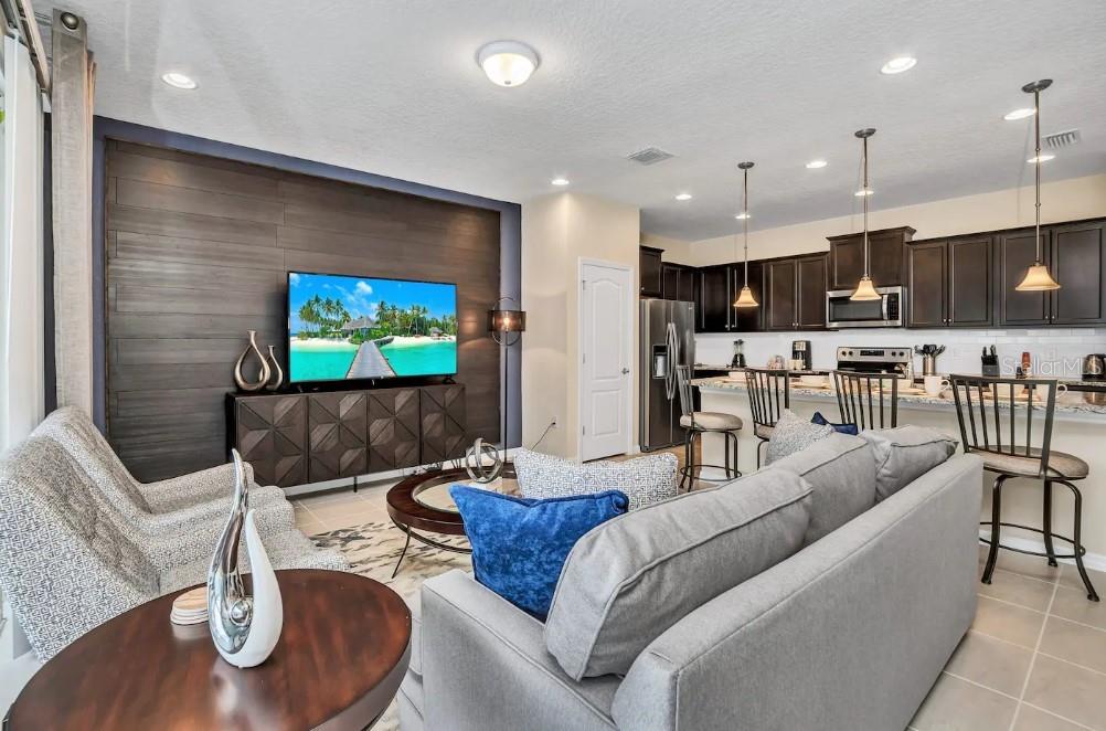 An open-concept living room and kitchen featuring dark wood cabinetry and a wood-paneled accent wall — 2407 DUBAI STREET, KISSIMMEE, FL