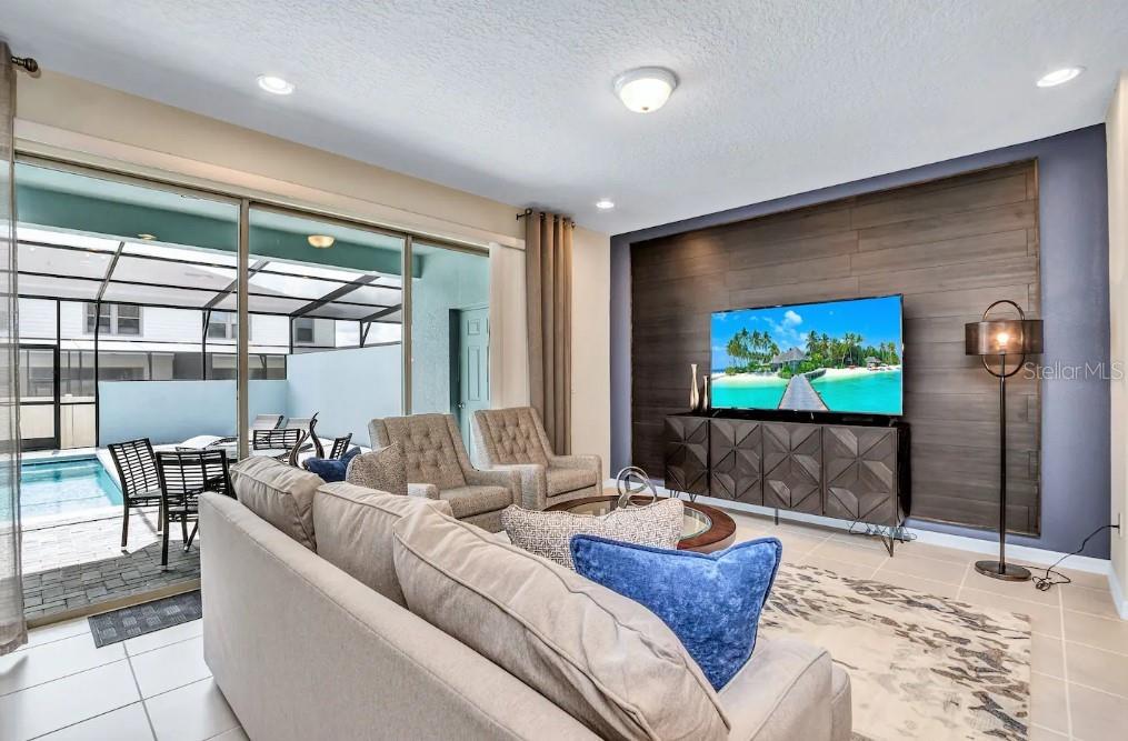 A living room features a wood-paneled accent wall, a television, and sliding doors to a pool — 2407 DUBAI STREET, KISSIMMEE, FL