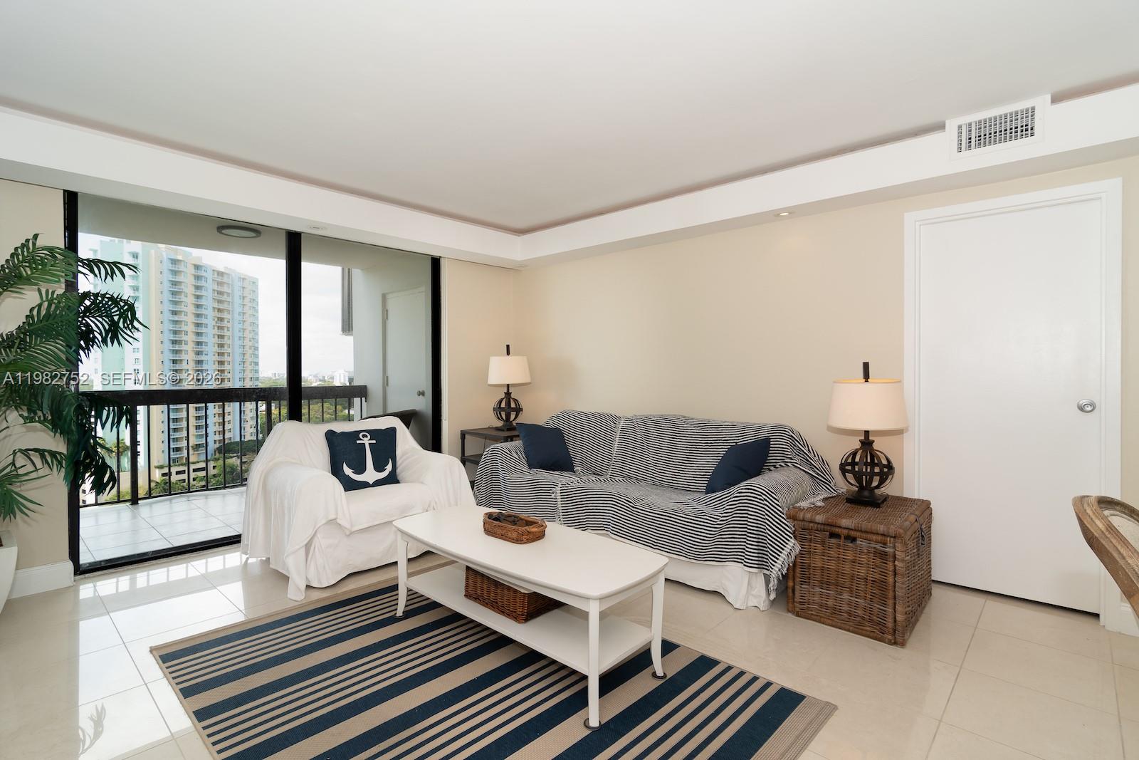 A living room features a striped sofa, white armchair, coffee table, and a balcony view — 2333 Brickell Ave # 1710, Miami FL 33129, MIAMI, FL