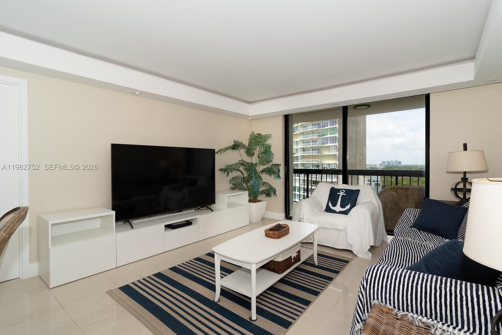 A living room features a television, white media console, striped rug, and balcony view — 2333 Brickell Ave # 1710, Miami FL 33129, MIAMI, FL