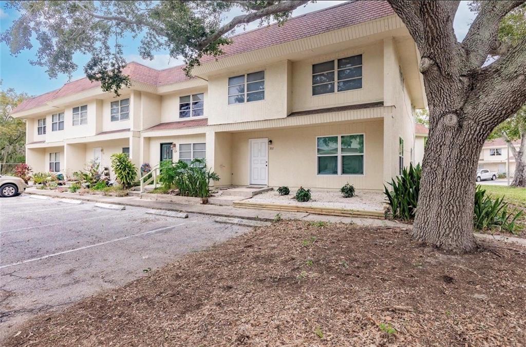 A two-story apartment building with beige stucco siding, a red roof, and a large tree — 331 AMHERST AVENUE UNIT 56, SARASOTA, FL