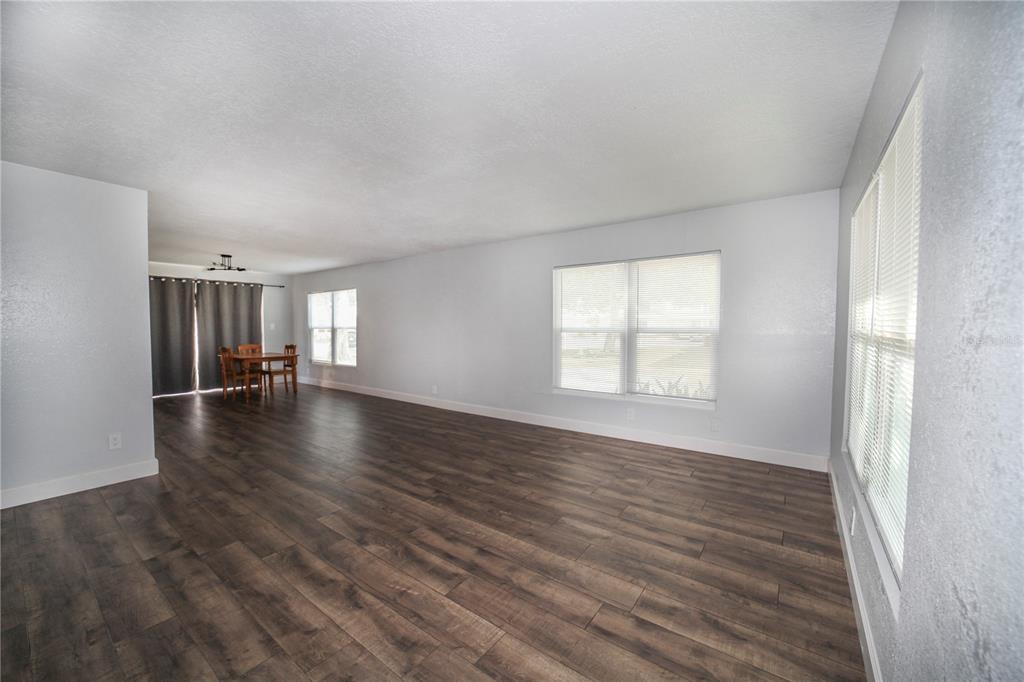A spacious living room with dark wood-look flooring, light gray walls, and multiple windows — 331 AMHERST AVENUE UNIT 56, SARASOTA, FL